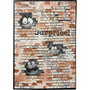 A rectangular printed card or poster with a brick-wall design, featuring three cartoon monster faces peeking through faux brick cutouts and the word 'Surprise!' in black text across the center.