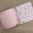 An open vintage-style planner or journal on a textured beige fabric background, showing a pinked page on the left and a sheet of decorative ticket stickers on the right with aged illustrations and text.