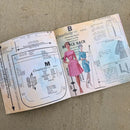 An open vintage sewing pattern booklet for Creativity 351 by B. Joyce Back, showing pattern measurements, garment sketches, and illustrated figures wearing dresses, placed on a textured beige fabric background.