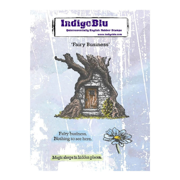 IndigeBlu 'Fairy Business' rubber stamp card featuring an illustration of a stone cottage with a tree trunk for a roof, a small flower, and decorative text on a distressed light blue background.