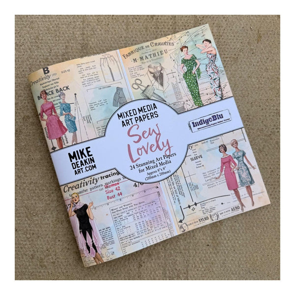 A packaged set of vintage-style mixed media art papers titled 'Sew Lovely' by Mike Deakin Art, shown on a textured beige fabric background. The paper pack features retro sewing illustrations of women in dresses and a central white label with pink and black text.