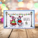 A rectangular Christmas greeting card featuring two cartoon mice in festive clothing under hanging holiday lights, with the text 'Christmas Whiskers' on the right side. The card is photographed standing upright on a wooden surface against a softly blurred multicolored bokeh background.
