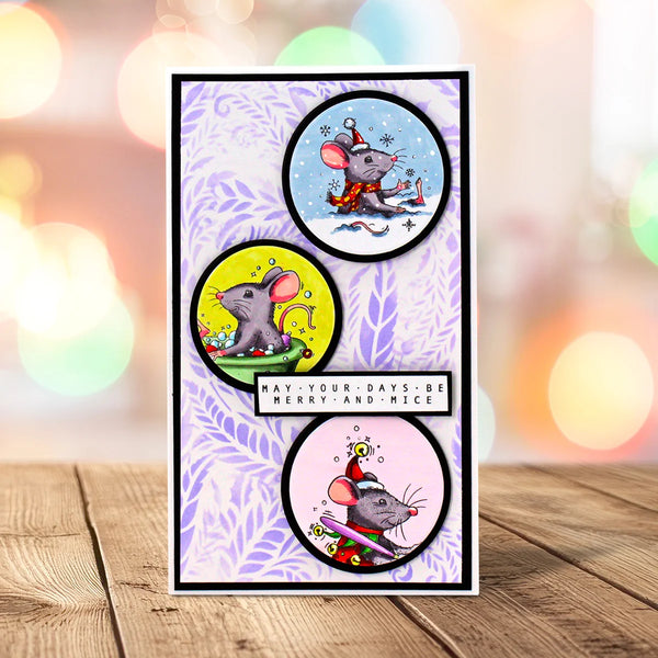 A handmade greeting card featuring three circular illustrations of cartoon mice in holiday poses, with a central banner reading 'HAY-YOUR DAYS BE MERRY AND NICE'. The card is displayed upright on a wooden surface with a blurred bokeh background.