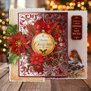 A handmade Christmas greeting card with a red and white ornate border, featuring a gold ornament with 'Merry Christmas' text, red poinsettias, pinecones, holly, and a robin bird illustration. The card is displayed on a wooden surface with a blurred Christmas tree and warm lights in the background.