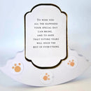 A white pet memorial plaque with a scalloped base and a central label containing a memorial quote, decorated with three orange paw print stickers.