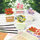 Decorative greeting cards with floral designs on a wooden surface with greenery in the background.
