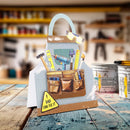 A decorative gift card shaped like a work apron filled with hand tools, displayed on a rustic wooden table with blurred paint cans and shelves in the background.
