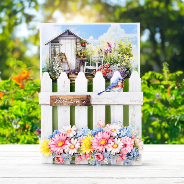 Greeting card with garden scene, flowers, and a bird on a white picket fence.