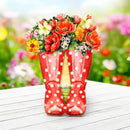 Red polka dot boots with a floral arrangement on a wooden surface with a garden background