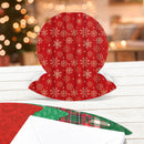 Red snowman-shaped card with white snowflakes on a wooden surface with a blurred Christmas tree background.