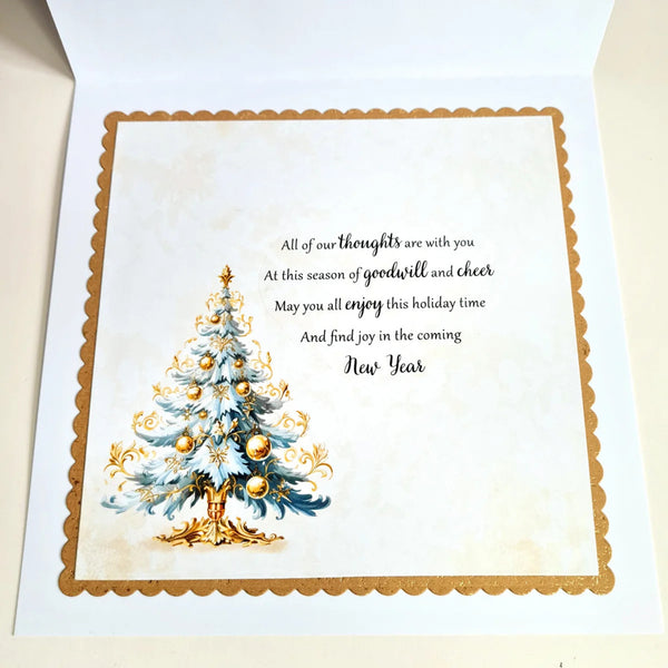 An open greeting card with a festive New Year design. The card features a watercolor-style decorated Christmas tree on the left and elegant black script text on the right that reads, 'All of our thoughts are with you.