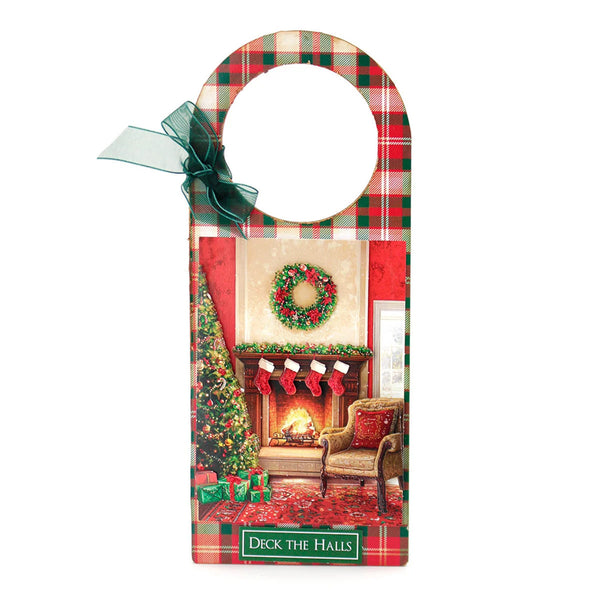 A Christmas-themed wooden hanging sign with a hanger loop at the top, featuring a red and green plaid border, a green ribbon bow, and a central printed holiday scene of a decorated fireplace, wreath, tree, stockings, and a chair. The sign reads 'Deck the Halls' at the bottom.