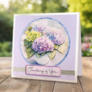 Greeting card with hydrangea design and 'Thinking of You' message on a wooden surface with blurred greenery background.