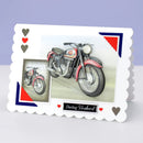 A scalloped-edge greeting card featuring a vintage red motorcycle illustration and a smaller inset photo of the same motorcycle. The card has heart suit symbols in red and gray in the upper left and a black banner at the bottom reading 'Darling Husband' with small red hearts.