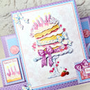 A colorful handmade birthday card featuring a 3D-style layered cake with candles, bows, strawberries, and decorative borders, shown alongside matching card elements on a light textured background.