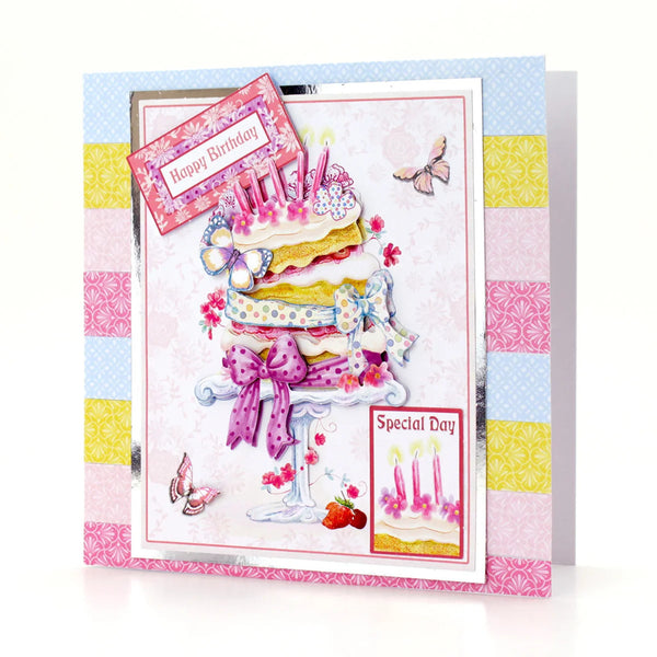 A handmade layered card featuring a 3D cake with candles, butterflies, strawberries, and decorative patterned borders in pastel pink, blue, yellow, and white. The card includes text elements reading 'Happy Birthday' and 'Special Day'.
