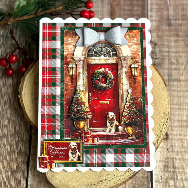 A scalloped holiday greeting card featuring a festive front door scene with a red door, wreath, garlands, plaid borders, and a small dog portrait. The card is photographed on a rustic wood surface with evergreen branches and red berries nearby.