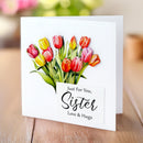 Greeting card with colorful tulips and 'Just For You, Sister Love & Hugs' text on a wooden surface.