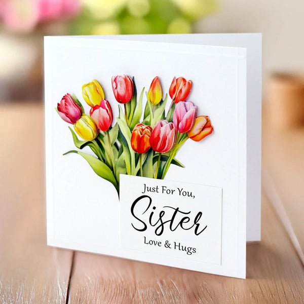 Greeting card with colorful tulips and 'Just For You, Sister Love & Hugs' text on a wooden surface.