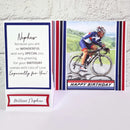 A folded birthday card shown open on a white surface against a white textured wall. The left panel has a white background with navy and red border accents and a message addressed to 'Nephew.