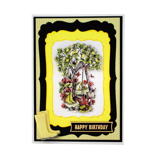 A handmade-style birthday card featuring a central illustration of a tree with green leaves and yellow fruit, surrounded by red flowers, gardening tools, and yellow rain boots. The card has layered black and yellow decorative borders with a yellow 'HAPPY BIRTHDAY' banner at the bottom.