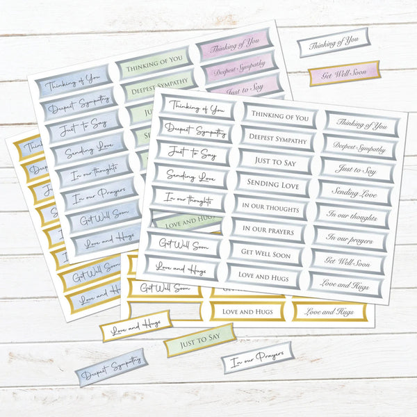 A set of printed sympathy and greeting sticker sheets arranged on a whitewashed wood background. The stickers are mostly light blue, gray, and lavender with gold borders and text such as 'Thinking of You,' 'Get Well Soon,' 'Love and Hang,' 'Just to Say,' and 'In my thoughts.