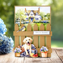 Greeting card with a dog, flowers, and a house on a wooden surface with a blurred green background.