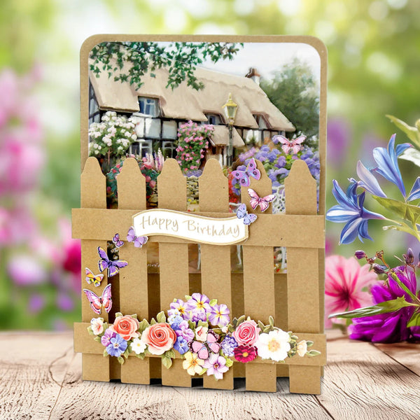 Decorative birthday card with a wooden fence design, flowers, and a village scene in the background.