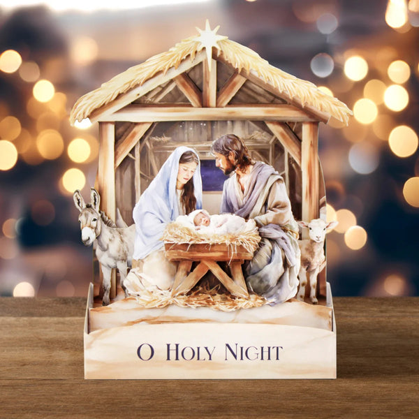 Nativity scene with 'O Holy Night' text on a wooden table with blurred lights in the background