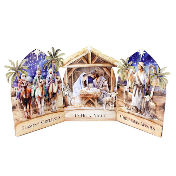 A three-panel nativity scene tabletop decoration on a white background. The center panel shows the Holy Family in a stable with the text 'O Holy Night,' while the left panel depicts three wise men with camels and the text 'Seasons Greetings,' and the right panel shows the Magi with sheep and the text 'Christmas Wishes.