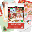 A festive card-making kit package labeled 'Santa & Friends Pop Up Christmas Card Making Kit' surrounded by sample holiday card designs and stickers, including Santa, penguins, gingerbread houses, elves, reindeer, and candy canes.