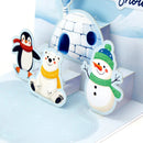 A 3D pop-up winter-themed card or decorative display featuring cartoon penguins, a polar bear, and a snowman in front of a white igloo on a snowy blue background.