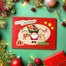 A festive Christmas greeting card with a red border and cartoon illustrations of Santa Claus, an elf, a reindeer, and wrapped gifts, placed on a green background with holiday decorations like pine branches, ornaments, and string lights.
