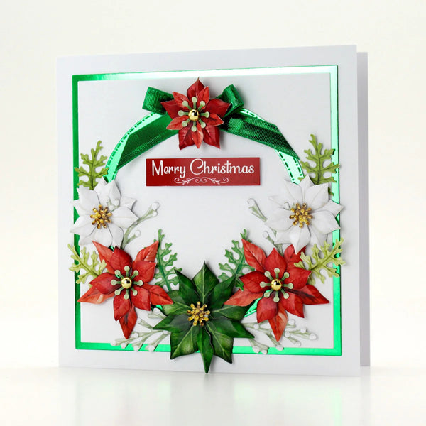 A square white greeting card with a 3D layered Christmas wreath design, featuring red poinsettias, white flowers, green leaves, a green ribbon bow, and a central red banner that reads 'Merry Christmas'.