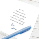 A white printed card with a condolence message in black script and a blue handwritten signature, placed on a light wood surface with a blue pen resting across the lower part of the card.