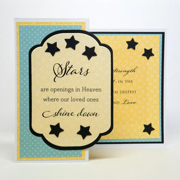 A handmade memorial or sympathy card with layered paper designs, featuring a central cream scalloped label with black script text reading 'Stars are openings in Heaven where our loved ones Shine down,' surrounded by black star cutouts. The card has a turquoise and yellow patterned background.