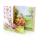 A set of personalized dog birthday cards shown standing upright on a white background. The cards feature watercolor-style illustrations of golden retrievers and corgis in outdoor picnic scenes, with one card displaying a red-and-white checkered banner that reads 'WITH LOVE TODAY & ALWAYS' and another card reading 'Happy Birthday'.