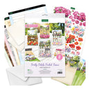 Kester's 'Pretty Petals Picket Fence' card making kit shown with its contents, including floral sticker sheets, cardstock, envelopes, and printed sample cards, arranged on a white background.
