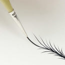A close-up of a fine liner eyeliner pen being used to draw a sharp, thin black line on a plain white surface.