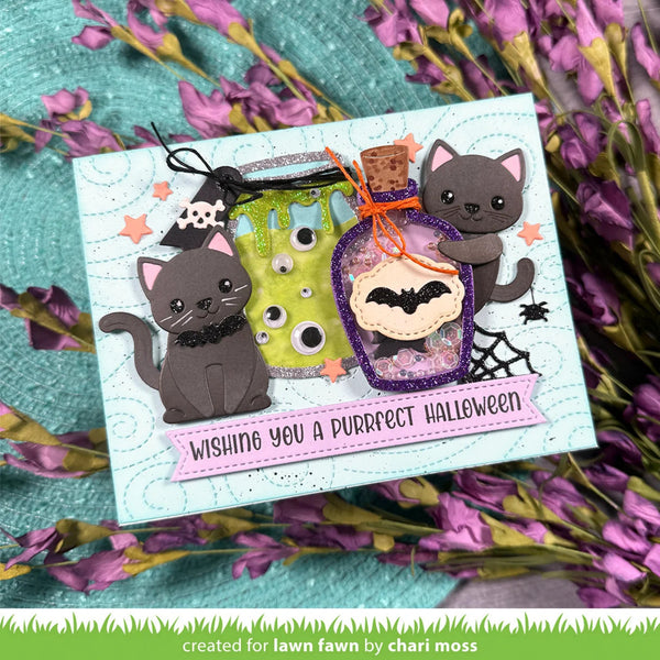 A handmade Halloween greeting card featuring two gray cats, a green cauldron, a purple potion bottle with a bat, and a pink banner reading 'Wishing you a purrfect Halloween.' The card is styled on a teal textured surface with purple flowers around it.