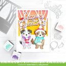 A handmade holiday greeting card featuring two cartoon dogs in winter clothing under a colorful striped arch with the words 'Season's Greetings.' The card is styled on a white surface with die-cut embellishments, stamps, and ink pads around it.
