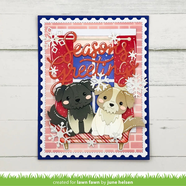 A handmade layered greeting card featuring two cute paper dogs sitting in a sleigh under a red 'Seasons Greetings' script, with white snowflakes and a pink brick pattern background, displayed on a white wood plank surface.