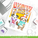A handmade layered card featuring two cute cartoon dogs wearing winter hats and scarves under a 'Season's Greetings' banner. The card is styled on a white surface with crafting tools, stamps, and ink pads around it.