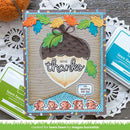 A handmade autumn-themed greeting card featuring an acorn, colorful leaves, the words 'GIVE thanks', and small cartoon squirrels, styled on a rustic wood surface with lace doilies and Lawn Fawn ink pads visible around it.