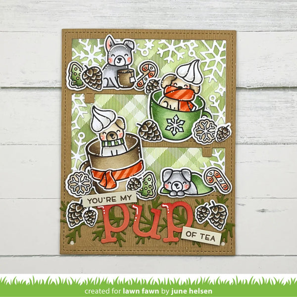 A handmade greeting card featuring cute cartoon dogs drinking tea in teacups, decorated with pinecones, snowflakes, and the text 'YOU'RE MY PUP OF TEA'. The card is displayed on a white wood panel background.