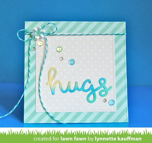 A handmade greeting card with a mint green and white striped border, a white polka-dot center panel, and the word 'hugs' in metallic gold and blue gradient lettering. A mint green and white twine bow with a pearl accent sits on the upper left.