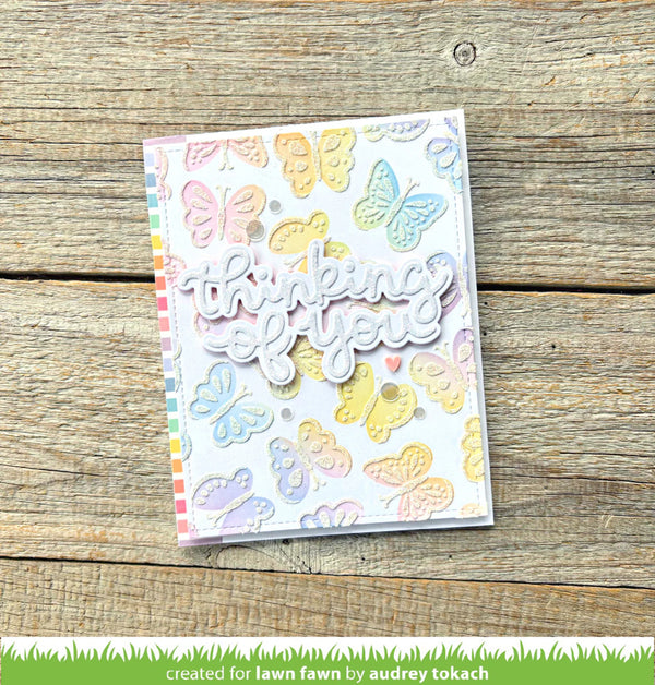Card with colorful butterfly designs and 'thinking of you' text on a wooden surface
