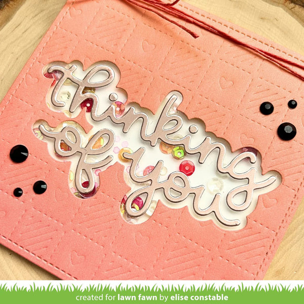 Pink card with 'thinking of you' text and decorative elements on a wooden surface.