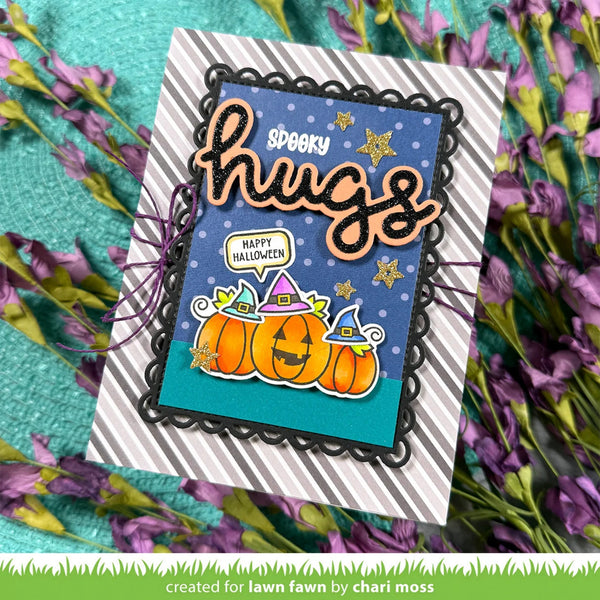 A handmade Halloween greeting card with 'spooky hugs' and 'Happy Halloween' text, featuring three jack-o'-lanterns with witch hats on a blue starry background. The card is displayed on a striped cardstock base and styled with purple flowers on a teal textured background.