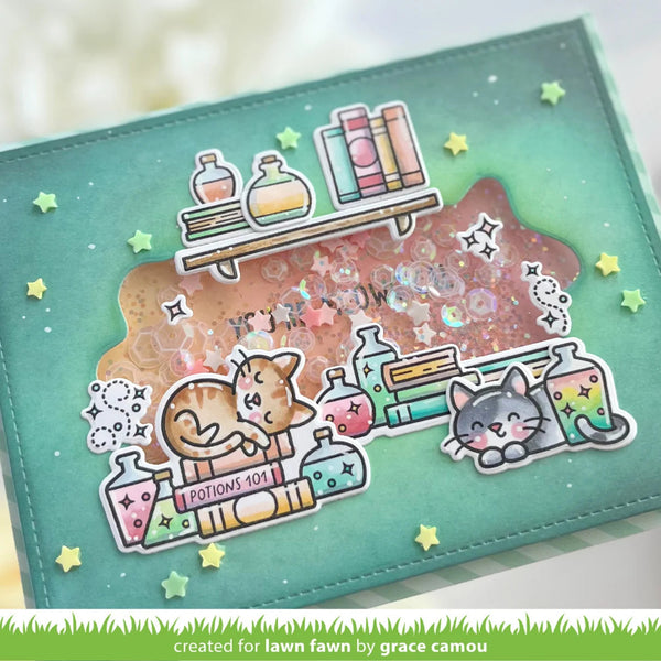 A handmade scrapbook card or journaling page featuring a teal background with a glittery pink central panel, cartoon cats, potion bottles, books, stars, and small yellow star accents. A watermark at the bottom reads 'created for lawn fawn by grace camou'.